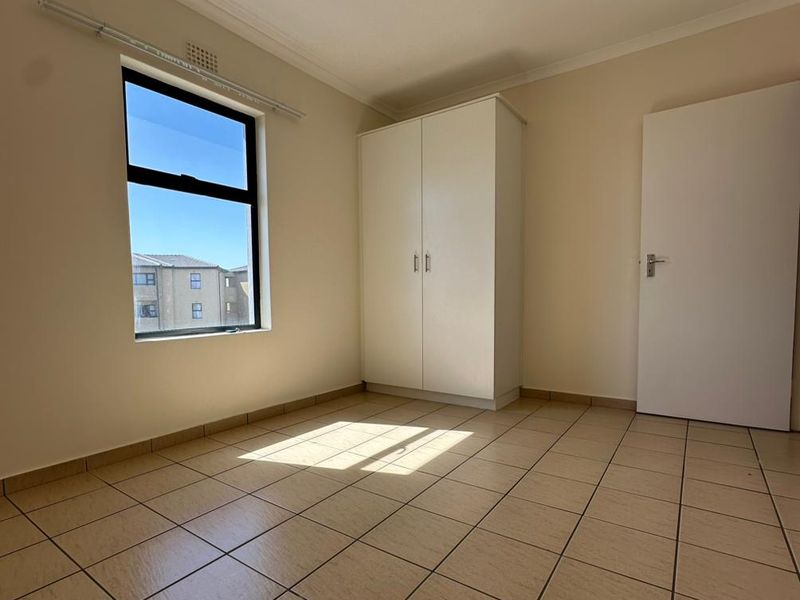 A bright, empty bedroom featuring neutral tiled flooring, a built-in wardrobe, and a window providing natural light.