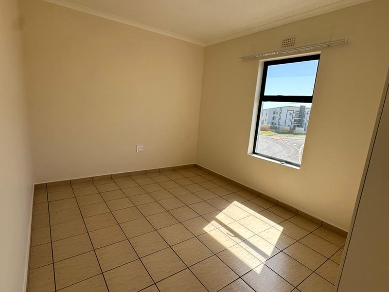 A clean, empty bedroom featuring neutral tiled flooring, a single window with a curtain rail, and a simple ceiling light fixture.