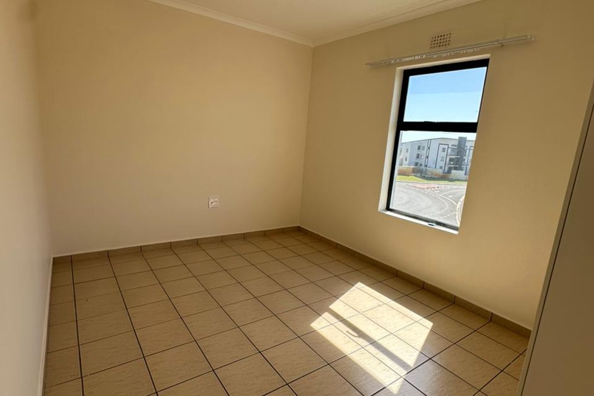 A clean, empty bedroom featuring neutral tiled flooring, a single window with a curtain rail, and a simple ceiling light fixture.