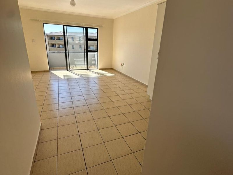 An empty, sunlit living area featuring neutral tiled flooring and a large sliding glass door providing access to an outdoor space.