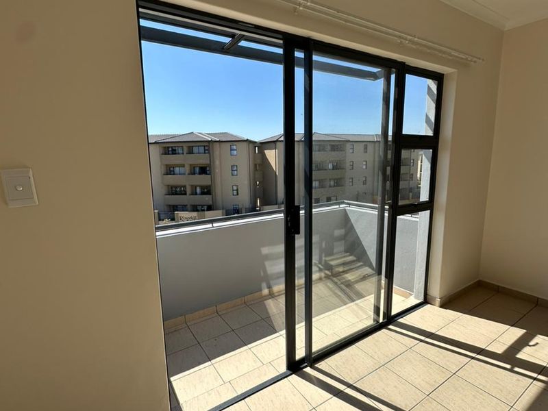 Bright and spacious living area featuring large sliding glass doors that open onto a private balcony with tiled flooring.