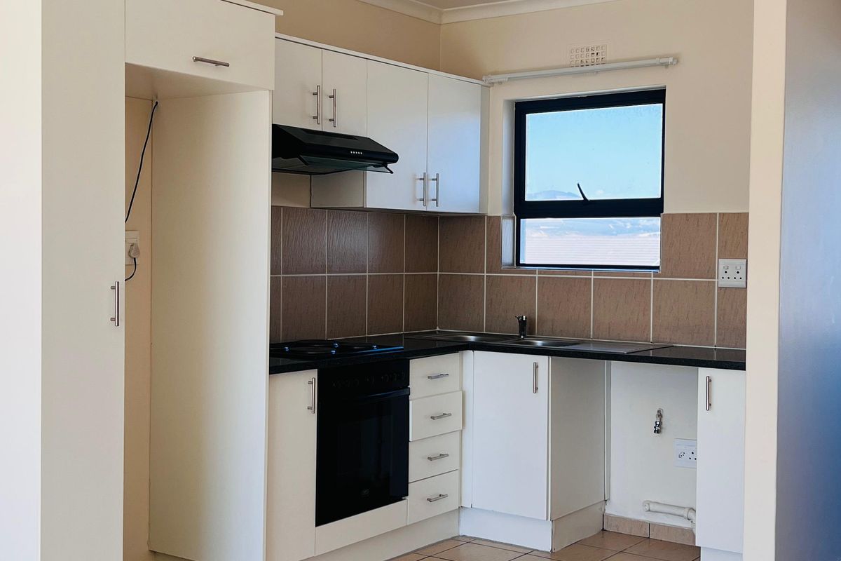 A clean, functional kitchen featuring white cabinetry, dark countertops, tiled splashbacks, and built-in oven and hob, presented in an empty, well-maintained space.