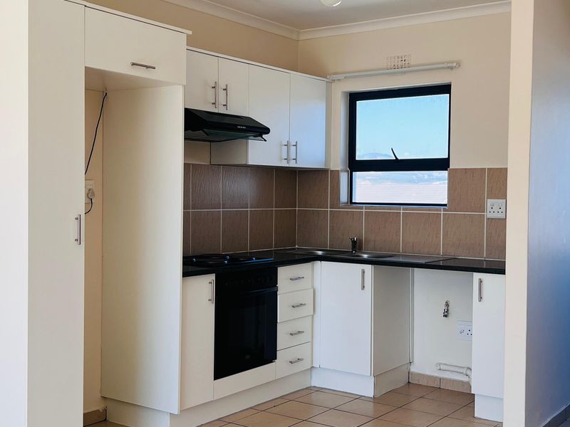 A clean, functional kitchen featuring white cabinetry, dark countertops, tiled splashbacks, and built-in oven and hob, presented in an empty, well-maintained space.