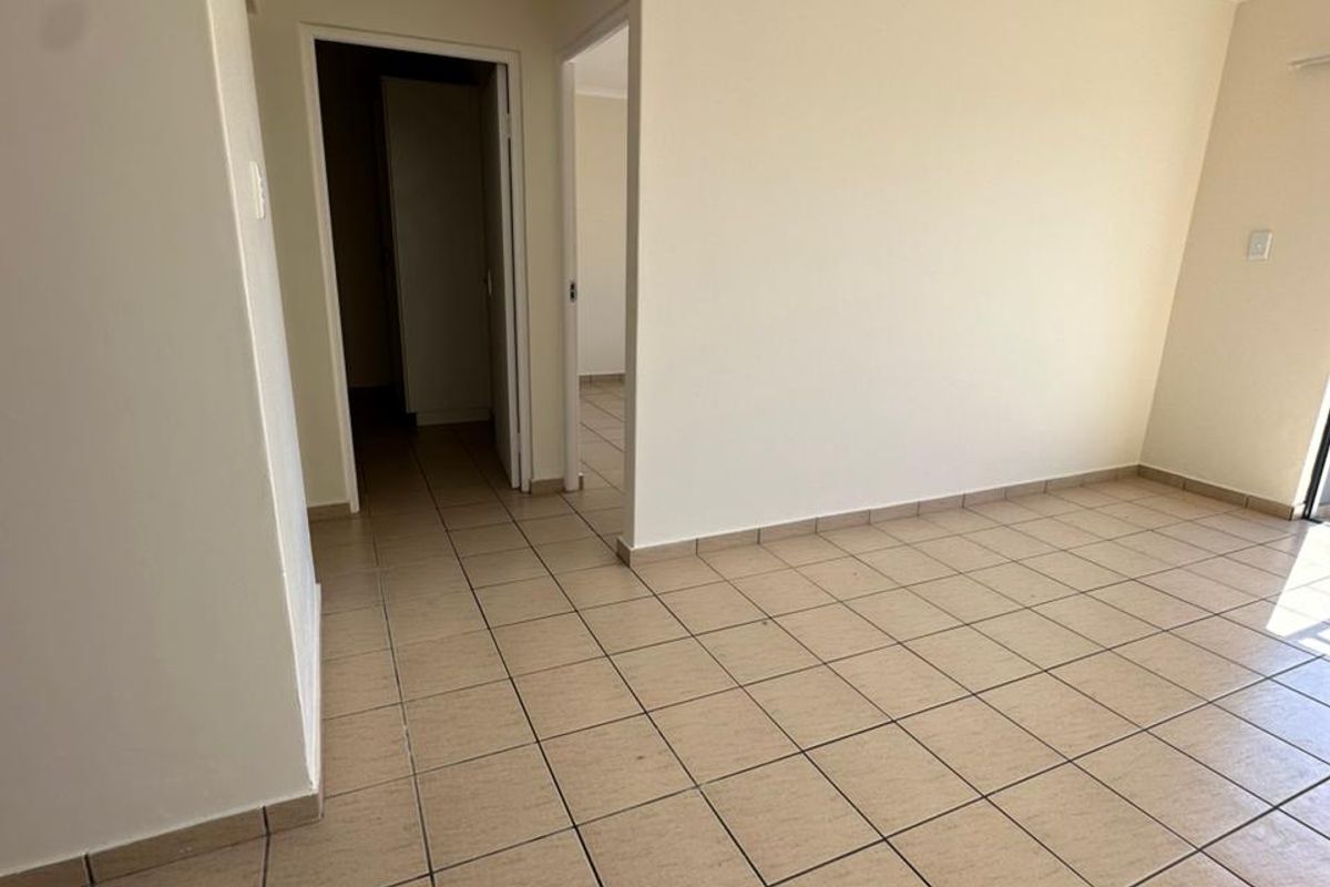 An empty, neutrally painted living area featuring ceramic floor tiles and access to a hallway, providing a blank canvas for interior design.