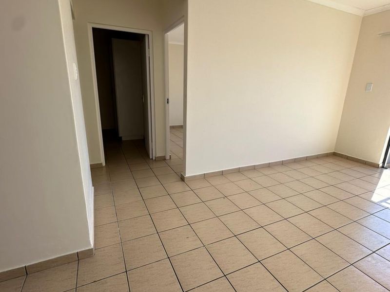 An empty, neutrally painted living area featuring ceramic floor tiles and access to a hallway, providing a blank canvas for interior design.