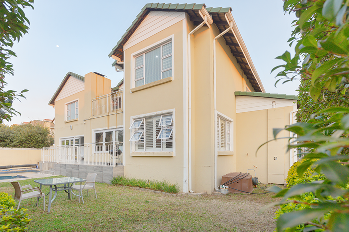 Rear view of a two-story residential property featuring a tiled roof, balcony, and access to a swimming pool area.