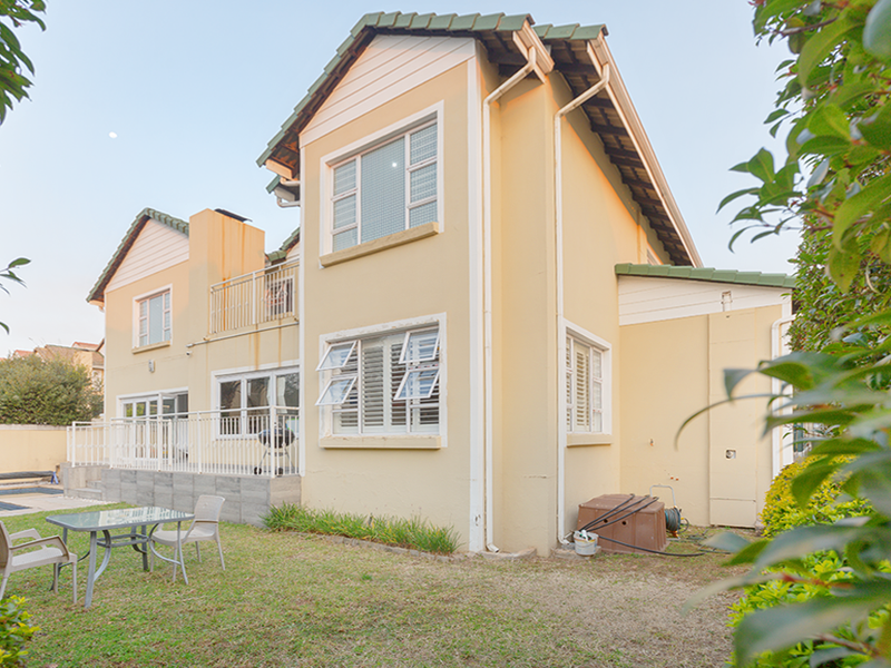 Rear view of a two-story residential property featuring a tiled roof, balcony, and access to a swimming pool area.