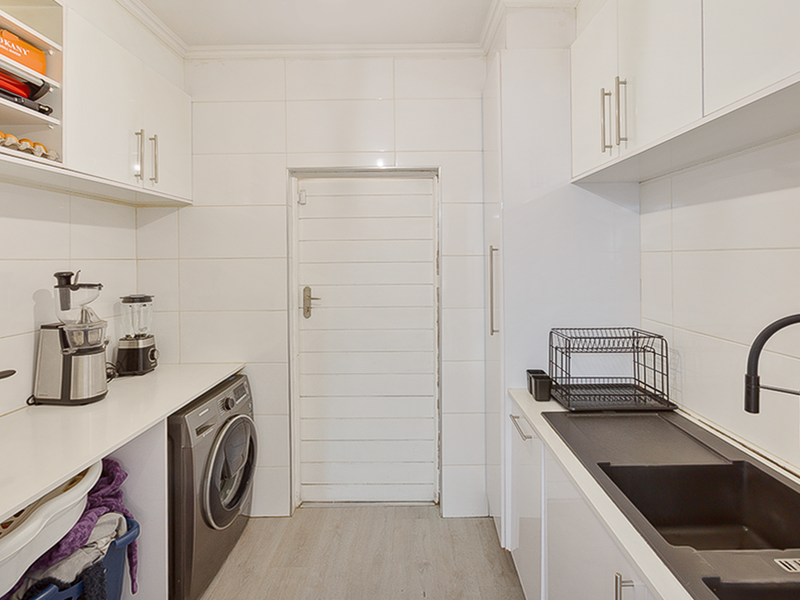 A functional scullery featuring white cabinetry, laminate countertops, a black composite sink with modern tapware, and space for laundry appliances.