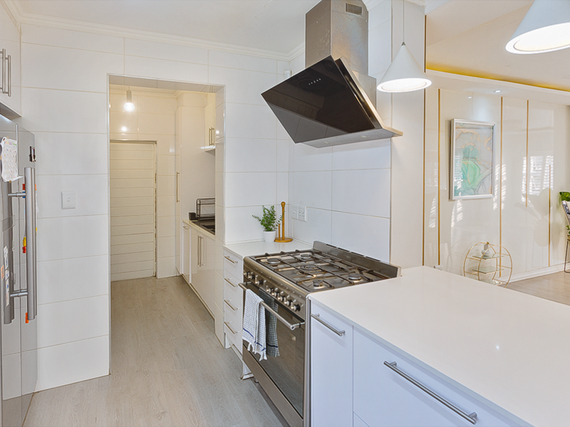 Modern kitchen featuring white cabinetry, stone countertops, gas stove with extractor fan, and tiled splashback, leading into a scullery area.