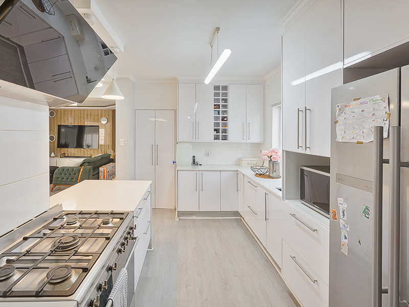 Modern kitchen featuring white high-gloss cabinetry, stone countertops, a gas hob with extractor, and integrated appliances, flowing into an open-plan living area.
