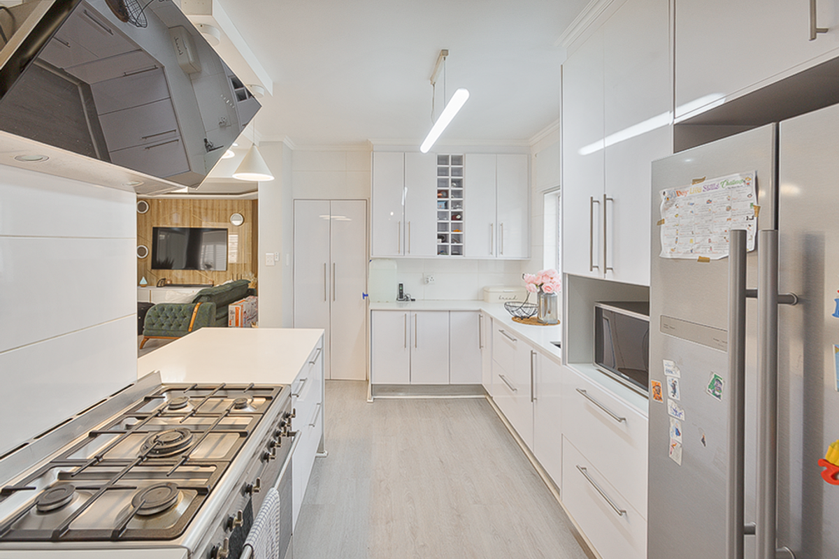 Modern kitchen featuring white high-gloss cabinetry, stone countertops, a gas hob with extractor, and integrated appliances, flowing into an open-plan living area.