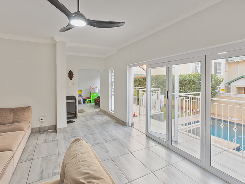 Bright living area featuring modern tiled flooring, a ceiling fan, and large aluminium stacker doors providing seamless access to the patio and pool area.