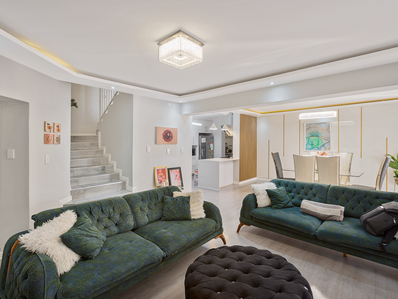 Spacious open-plan living and dining area featuring modern recessed lighting, a central staircase, and a sleek, contemporary kitchen with an island.