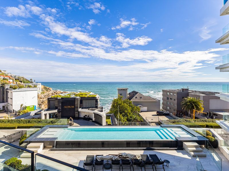 A luxurious elevated swimming pool area featuring modern glass balustrades and stone tiling, offering expansive ocean and coastal views.