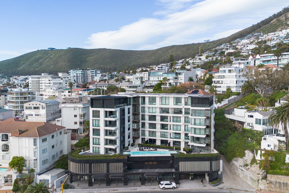 Aerial view of the Aurum apartment complex, showcasing its modern architectural design, balconies, and rooftop swimming pool in a coastal hillside setting.