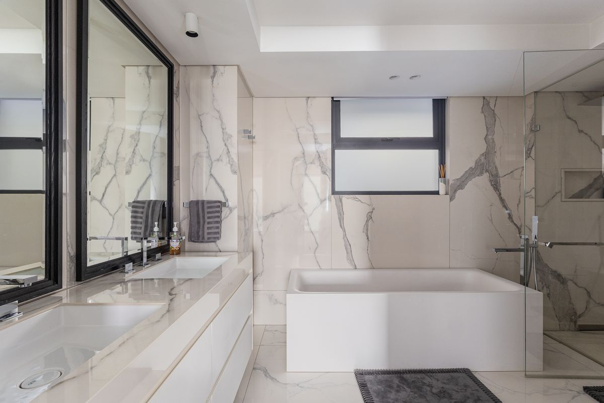 Modern luxury bathroom featuring a double vanity, marble wall and floor tiling, a built-in bathtub, and a separate glass-enclosed shower.
