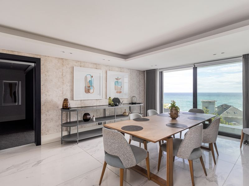 Elegant dining room featuring marble-look flooring, recessed ceiling lighting, and expansive floor-to-ceiling windows offering panoramic ocean views.