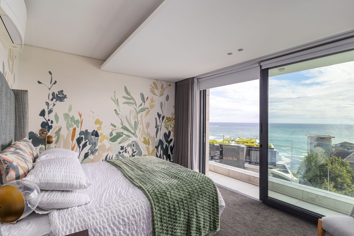 Modern bedroom featuring a large sliding glass door opening to a balcony with expansive ocean views and a decorative floral feature wall.
