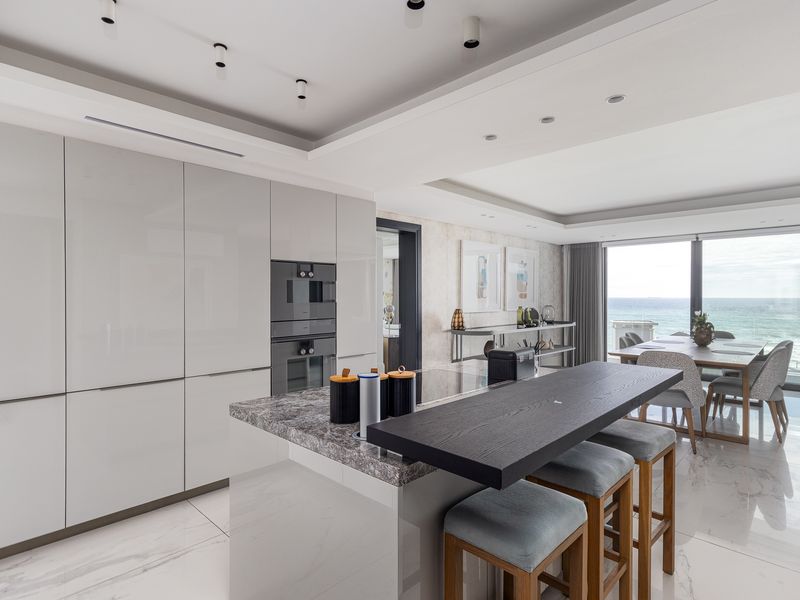 Modern open-plan kitchen and dining area featuring high-gloss cabinetry, stone island, and seamless access to a balcony with ocean views.