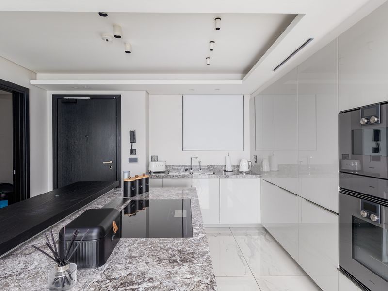 Modern kitchen featuring high-gloss cabinetry, stone countertops, integrated appliances, induction hob, and marble-effect flooring with recessed ceiling lighting.