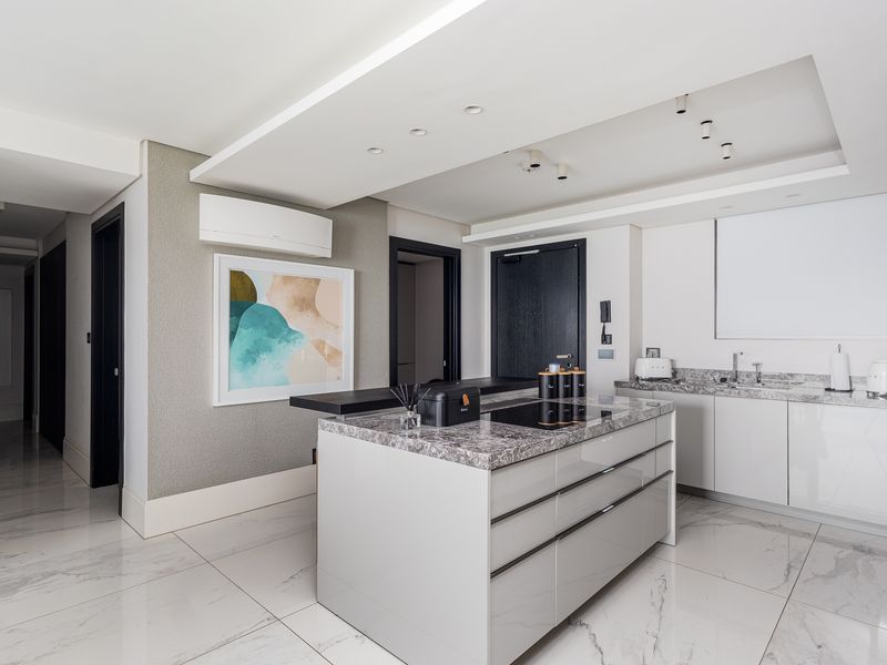 Modern kitchen featuring a central island with stone countertops, integrated hob, sleek cabinetry, and high-quality marble-look floor tiles in an open-plan layout.
