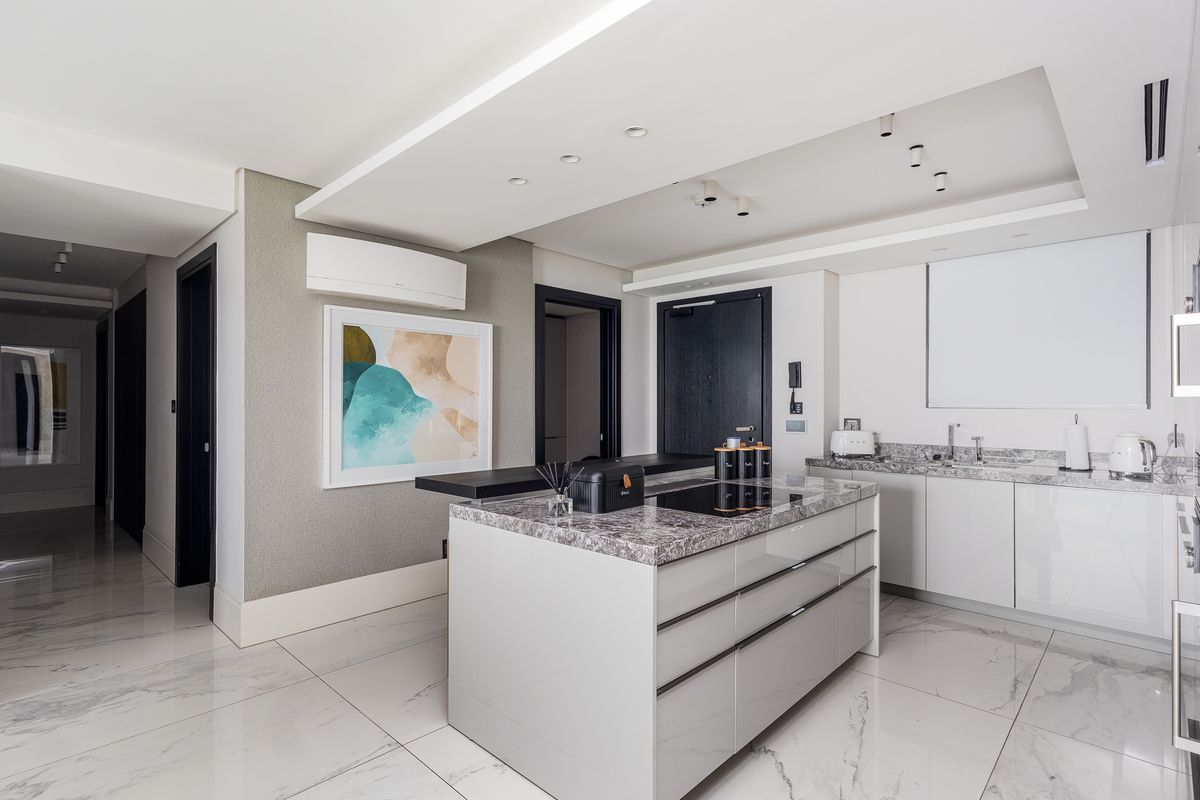 Modern kitchen featuring a central island with stone countertops, integrated hob, sleek cabinetry, and high-quality marble-look floor tiles in an open-plan layout.