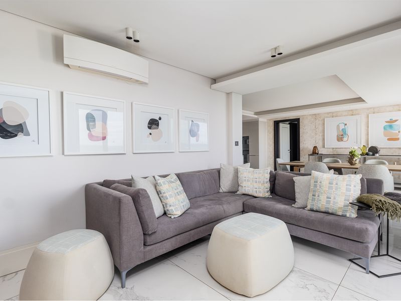 A bright and modern open-plan living and dining area featuring marble-look flooring, recessed ceiling lighting, and a wall-mounted air conditioning unit.