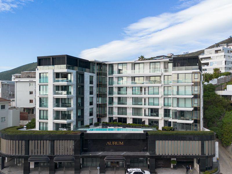 Modern multi-story apartment building featuring a rooftop pool, glass-fronted balconies, and contemporary stone facade architecture.