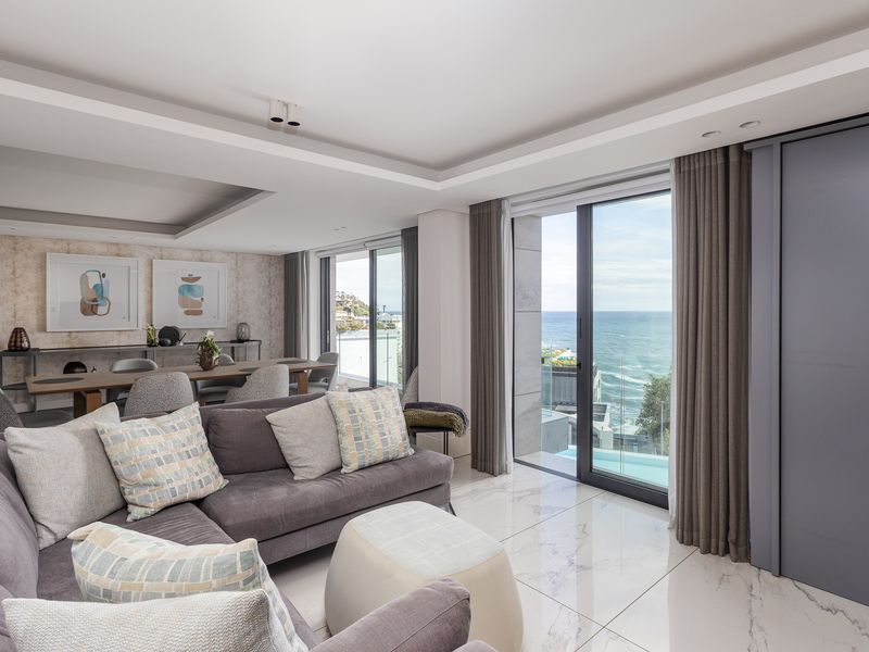 Spacious open-plan living and dining area featuring high-end marble flooring, recessed ceilings, and large sliding glass doors offering expansive ocean views.