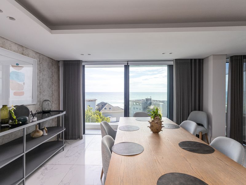 Modern dining area featuring marble-look flooring, recessed ceiling lighting, and floor-to-ceiling sliding doors offering expansive ocean views.