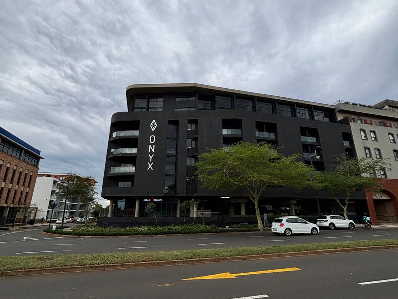 A modern multi-story apartment building exterior featuring a dark facade, prominent signage, and integrated balconies overlooking the street.