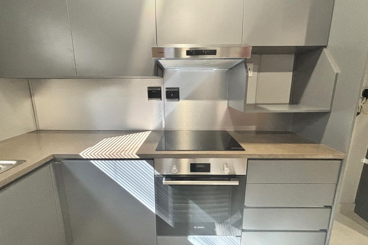 Modern kitchen featuring sleek grey cabinetry, stone countertops, stainless steel splashback, and integrated Bosch oven and hob.