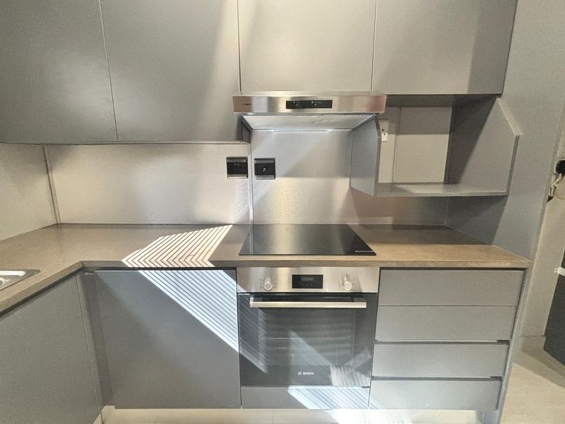 Modern kitchen featuring sleek grey cabinetry, stone countertops, stainless steel splashback, and integrated Bosch oven and hob.