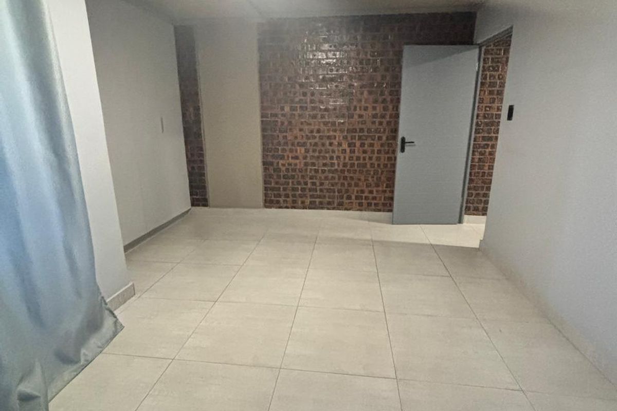 An empty bedroom featuring neutral tiled flooring and a distinctive exposed brick feature wall, providing a clean and versatile space.