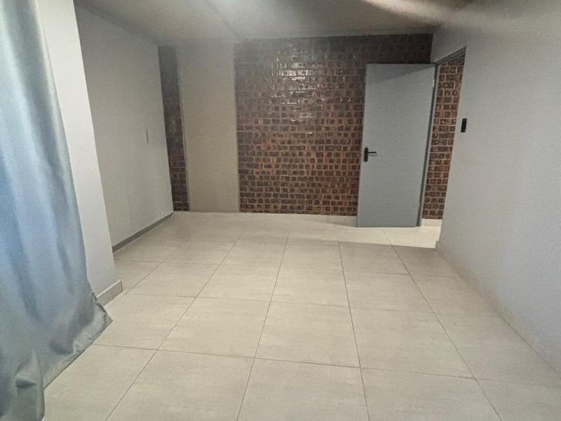 An empty bedroom featuring neutral tiled flooring and a distinctive exposed brick feature wall, providing a clean and versatile space.