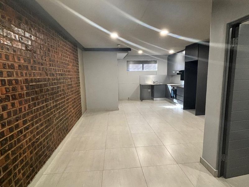 Spacious open-plan living and kitchen area featuring modern tiled floors, a striking exposed brick feature wall, and contemporary dark kitchen cabinetry.