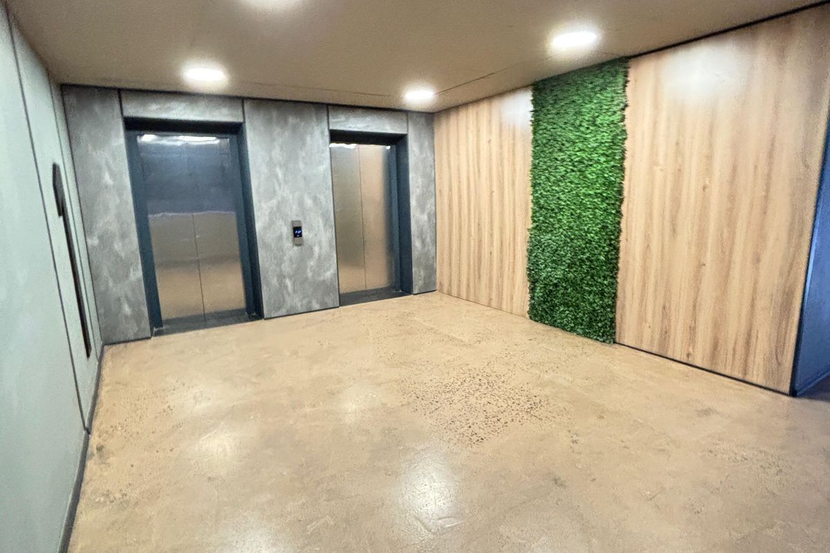 Modern apartment building lobby or hallway featuring dual elevators, polished concrete floors, and a decorative vertical garden wall.