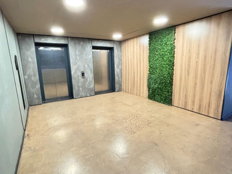Modern apartment building lobby or hallway featuring dual elevators, polished concrete floors, and a decorative vertical garden wall.