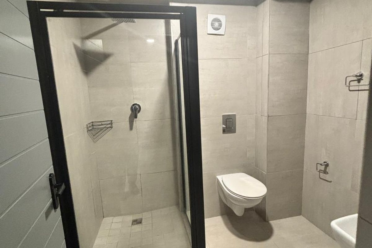 Modern bathroom featuring a walk-in shower with black-framed glass enclosure, wall-mounted toilet, and neutral floor-to-ceiling tiling.