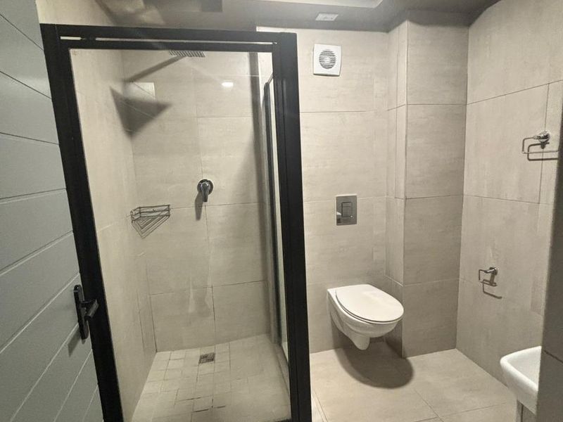 Modern bathroom featuring a walk-in shower with black-framed glass enclosure, wall-mounted toilet, and neutral floor-to-ceiling tiling.