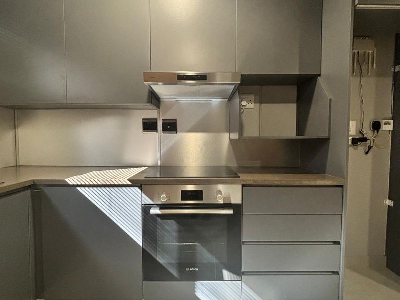 Modern kitchen featuring sleek grey cabinetry, stainless steel appliances including an oven and hob, and tiled flooring.