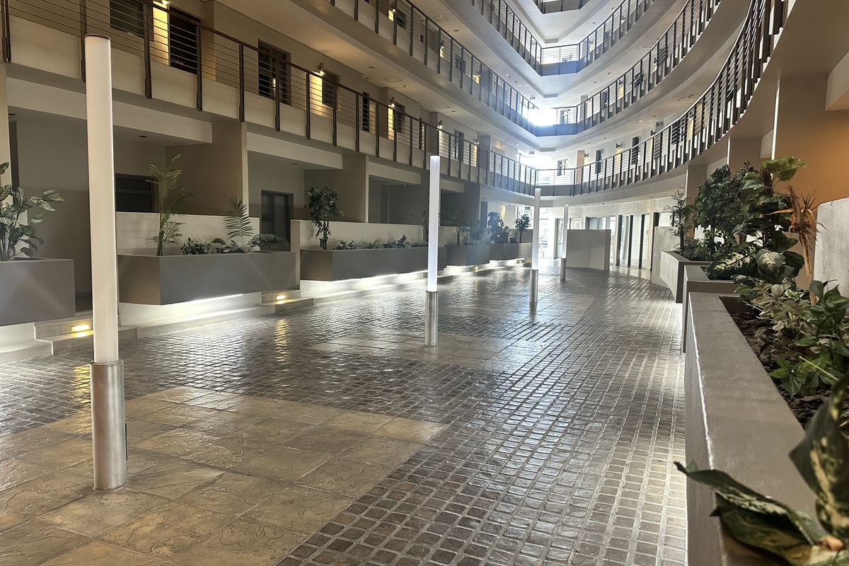 A modern, well-maintained apartment complex atrium featuring multi-level balconies, paved walkways, integrated lighting, and built-in planters.