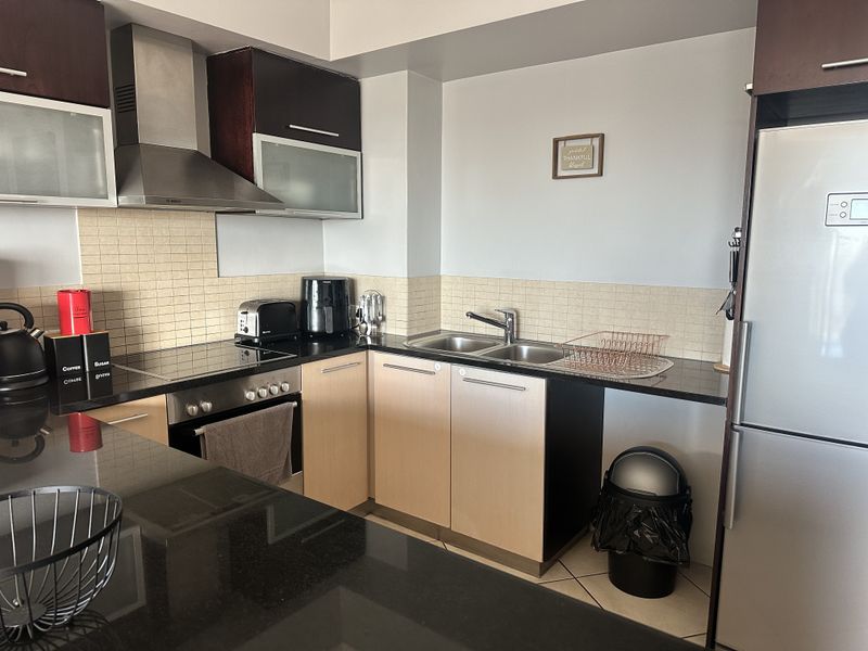 A functional kitchen featuring granite countertops, built-in oven, electric hob, stainless steel extractor fan, and ample cabinetry with a tiled backsplash.