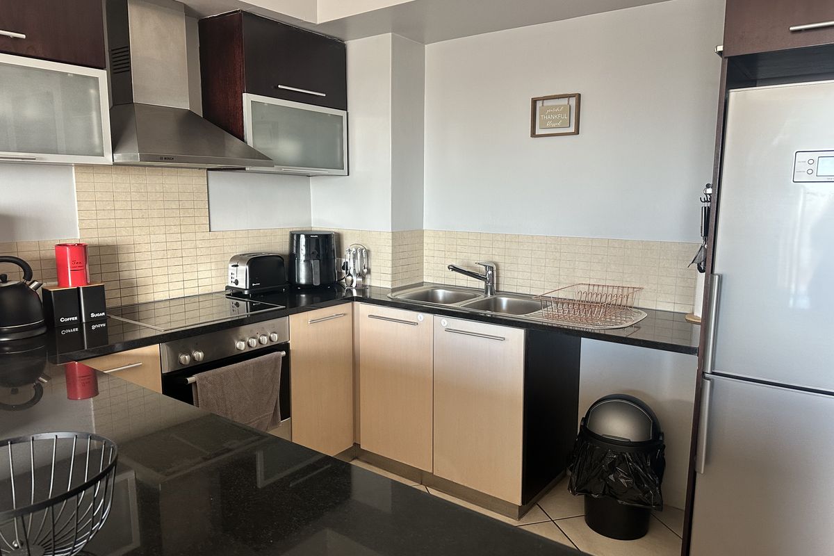 A functional kitchen featuring granite countertops, built-in oven, electric hob, stainless steel extractor fan, and ample cabinetry with a tiled backsplash.