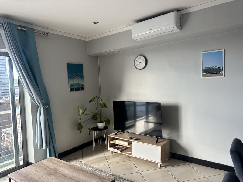 A well-maintained living room featuring tiled flooring, a wall-mounted split-system air conditioner, and a sliding glass door providing natural light.