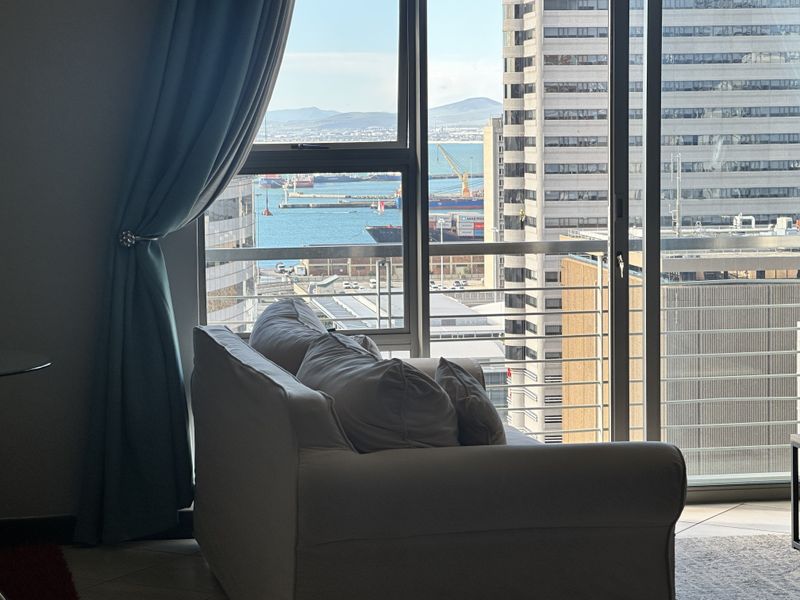 A view from an apartment interior looking out through large glass sliding doors towards the harbour and city skyline.