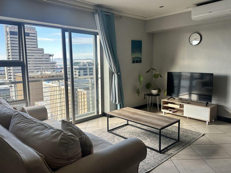 A bright living room featuring tiled flooring, a split-system air conditioner, and large sliding glass doors offering expansive city views.