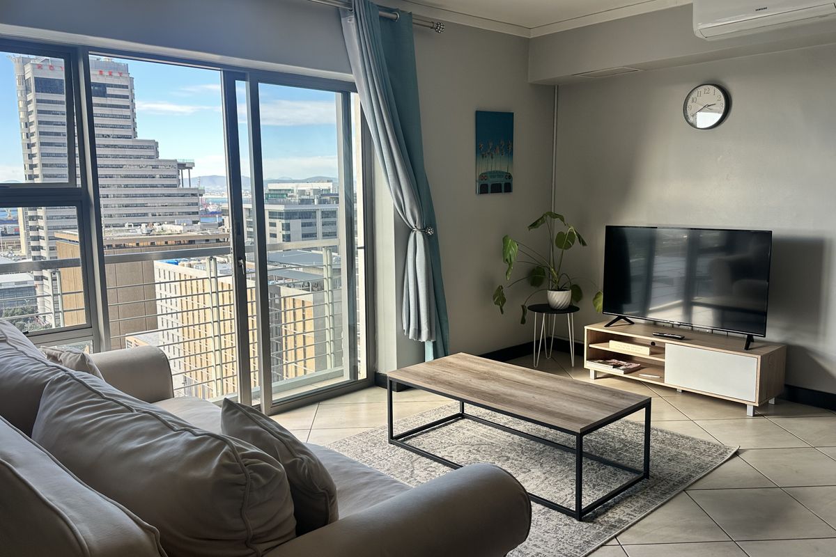 A bright living room featuring tiled flooring, a split-system air conditioner, and large sliding glass doors offering expansive city views.