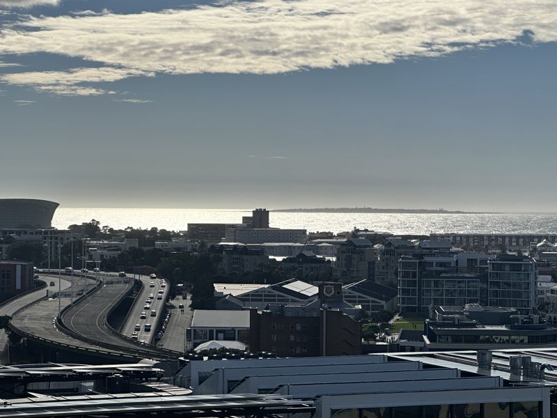 Elevated urban and coastal view overlooking the city skyline, highway infrastructure, and the ocean horizon.