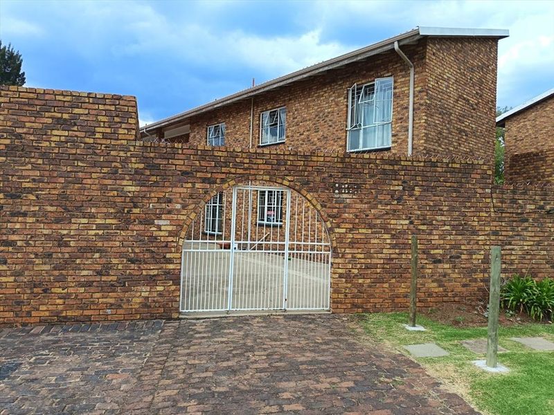 Front exterior view of a face brick townhouse featuring an arched metal security gate, paved driveway, and security bars on the windows.